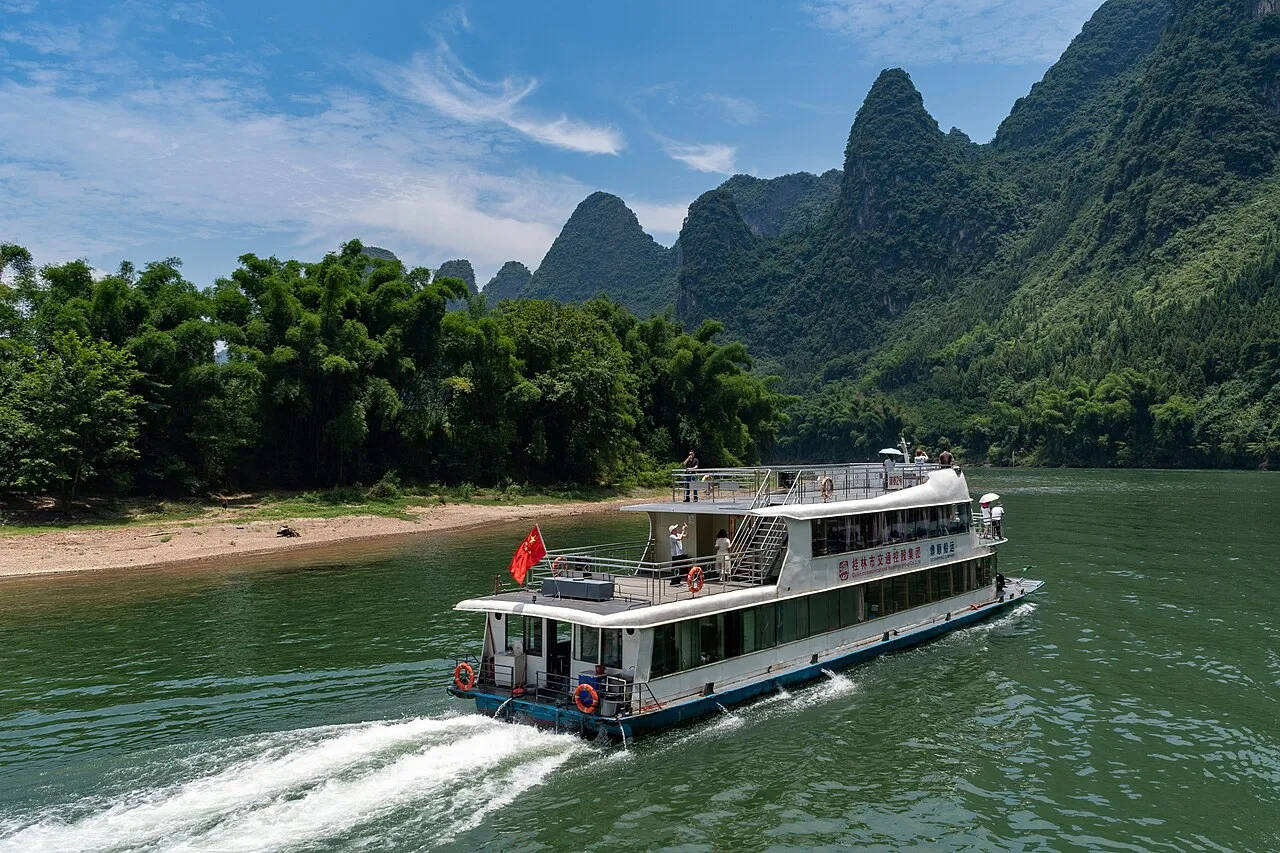 A two-deck passenger boat traveling on the Li River beside limestone peaks