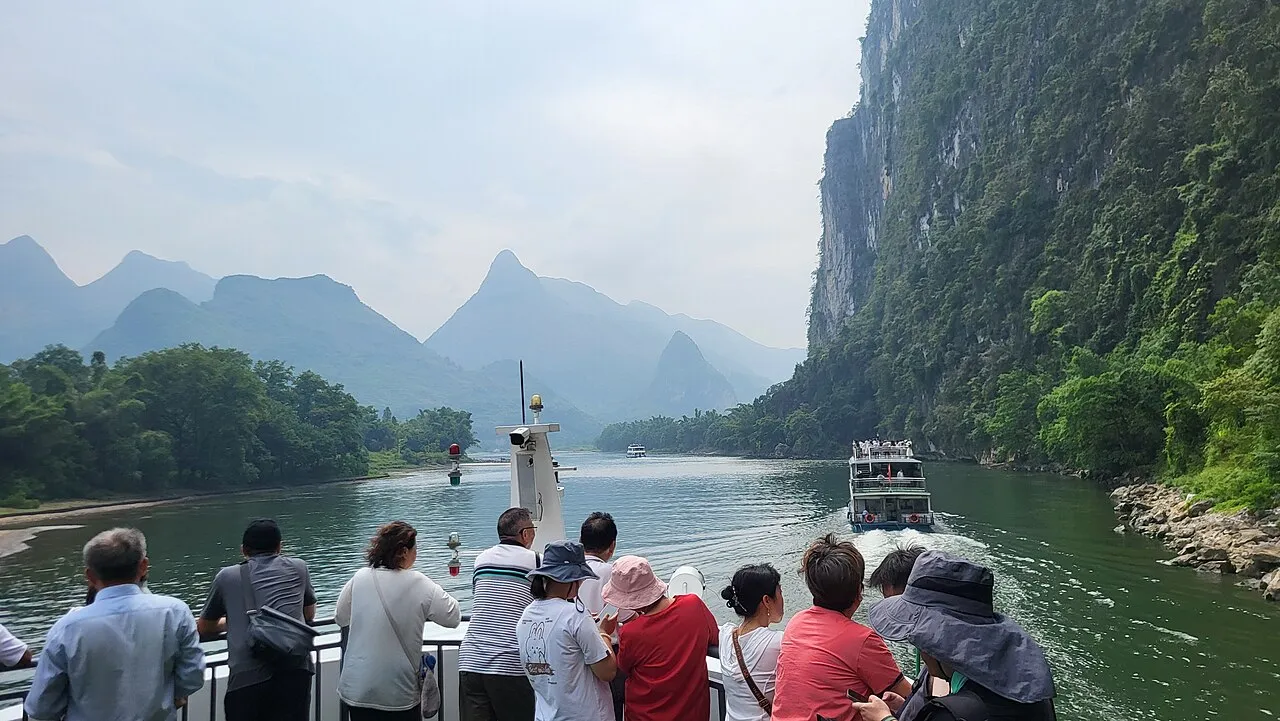 Passengers looking along the Li River from the open deck of a cruise boat between karst cliffs