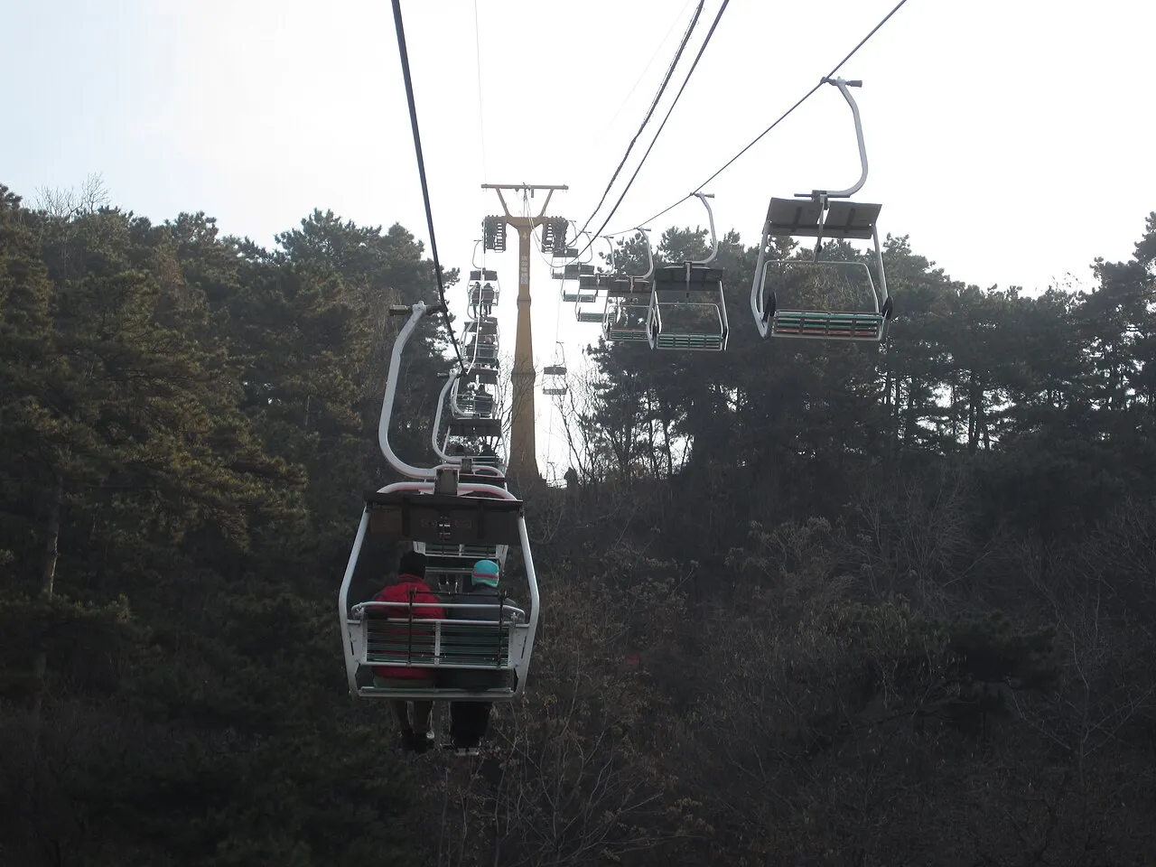 Open chairlift seats ascending the wooded hillside at Mutianyu