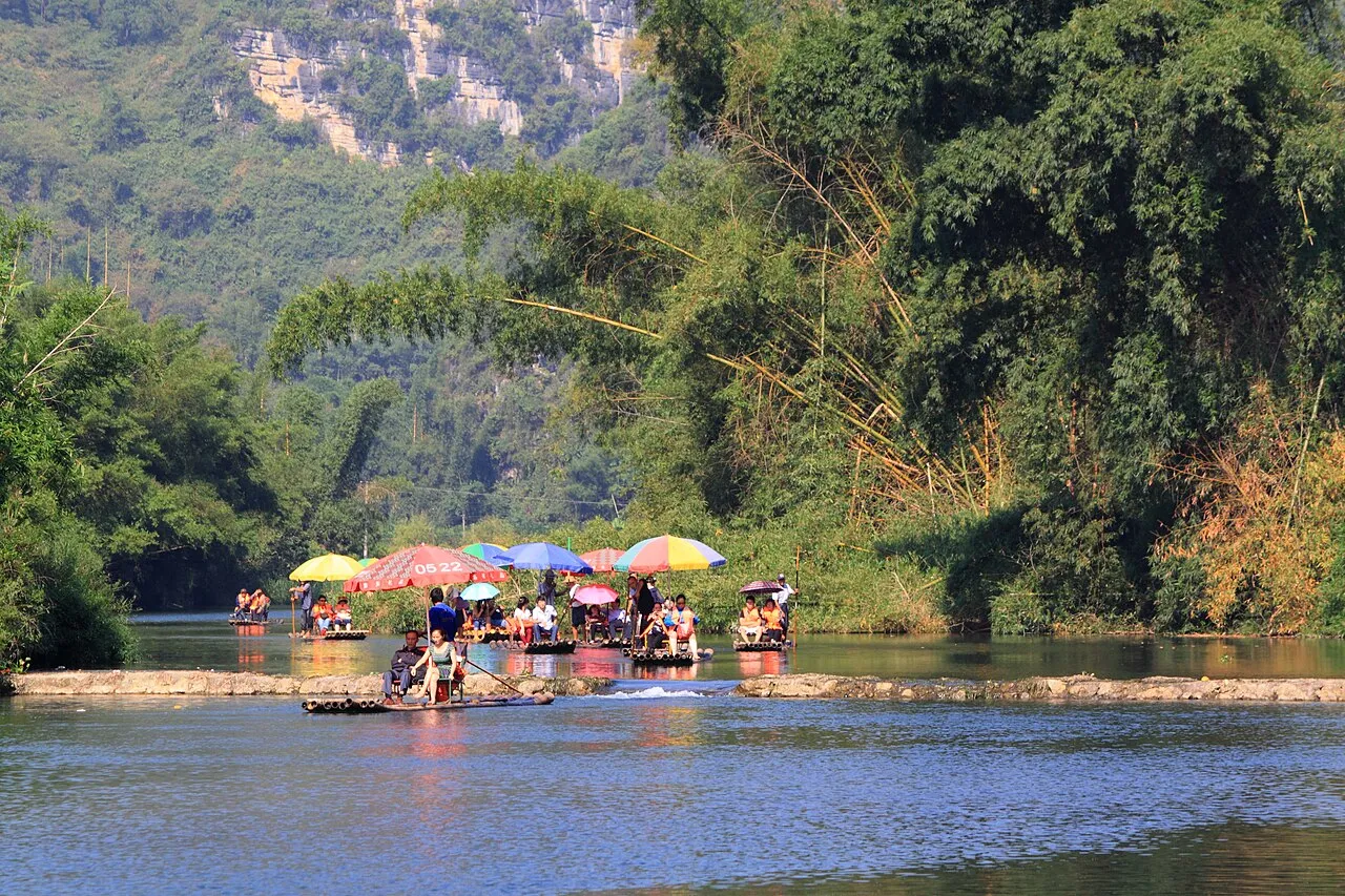A bamboo raft dropping over a low stone weir on the Yulong River