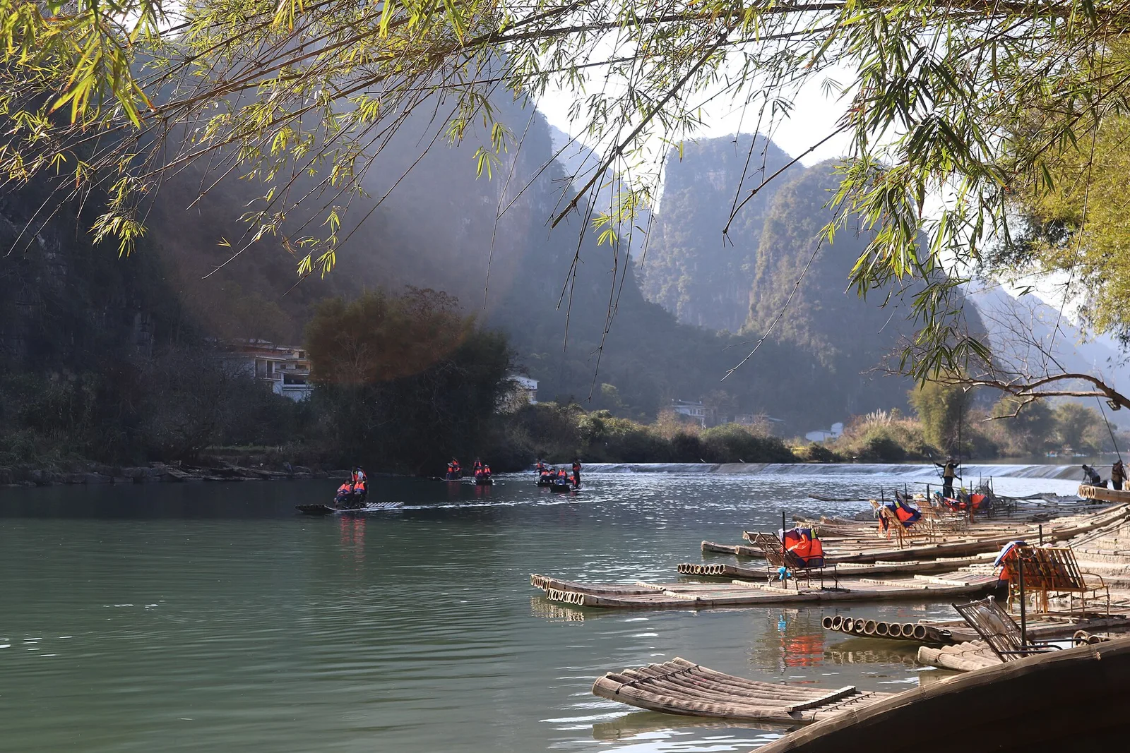 Bamboo rafts and riverside vegetation beneath limestone hills in the Yulong valley