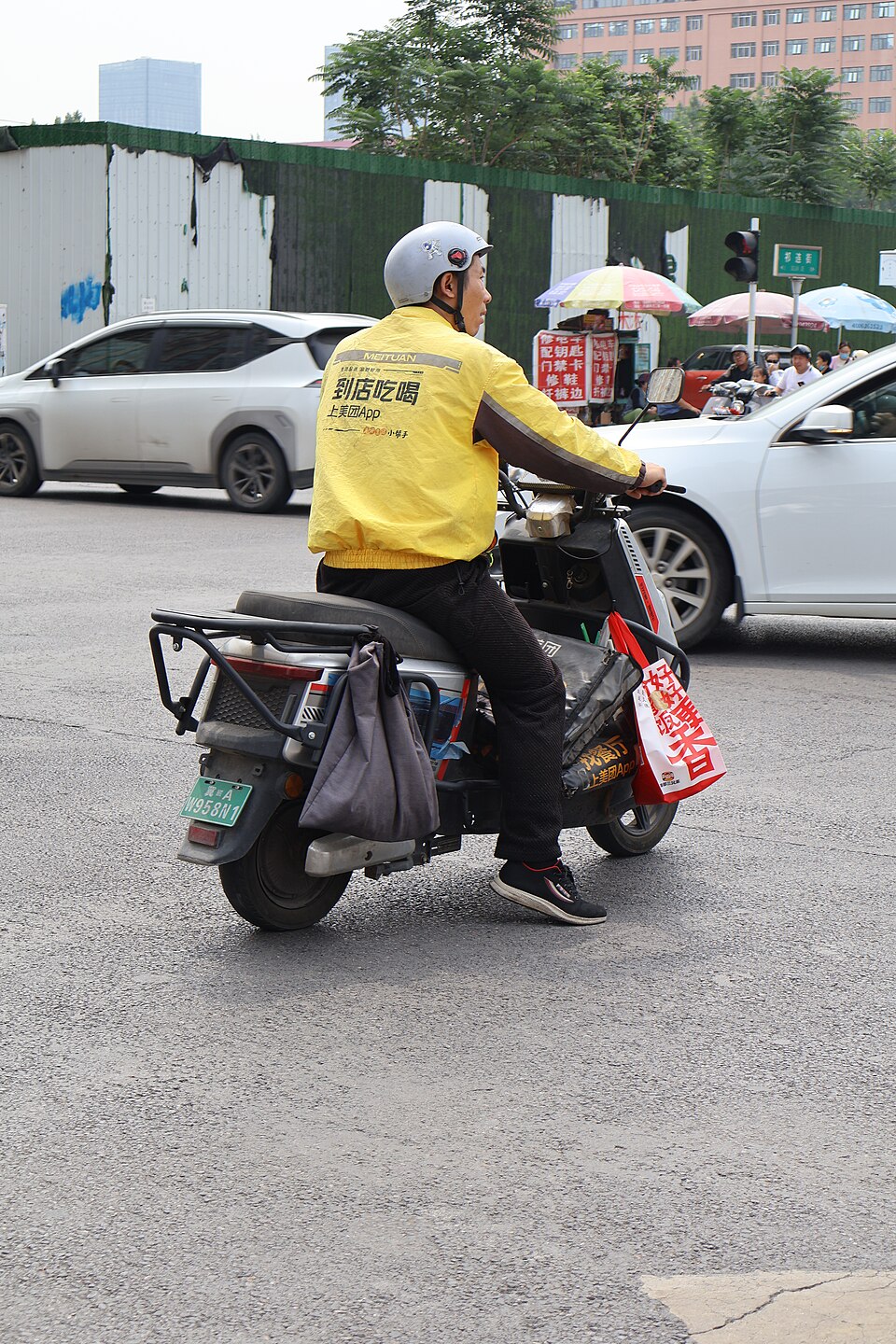 A Meituan food-delivery rider waiting on a scooter on a Chinese city street